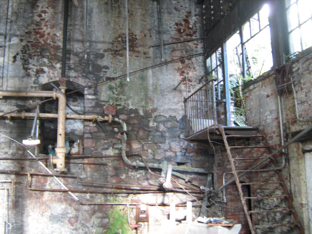 Photo from inside boiler house, showing dilapidated brick wall and steelstaircase coming down from broken windows