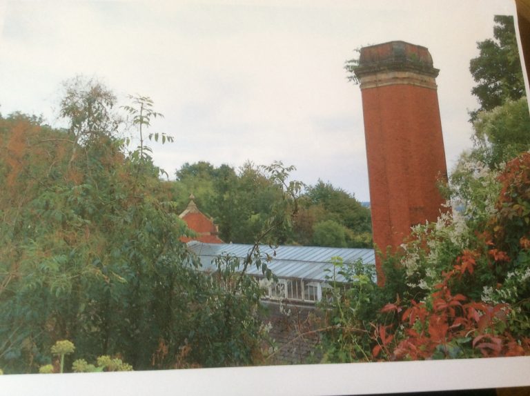 Photo of chimney and building in red brick with glazed roof, surrounded by trees