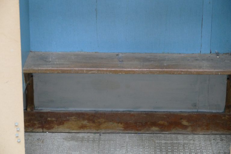 Photo of cubicle with wooden bench, blue wall and textured floor tiles
