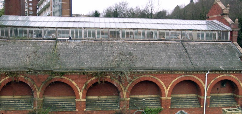 Photo of building from the side, showing pitched roof, glazed along thecentre, with tiled shoulders and red brick arches below